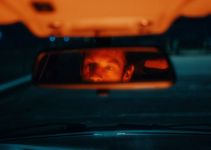 Man with focused expression seen in rearview mirror at night, illustrating quick reactions preventing a tragedy while driving.