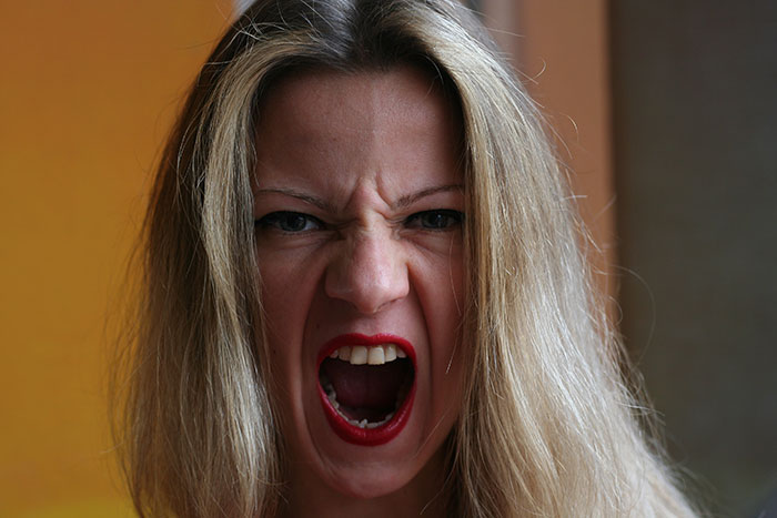 Close-up of a woman with blonde hair and red lipstick expressing intense rage, reflecting rage room customers needing therapy.