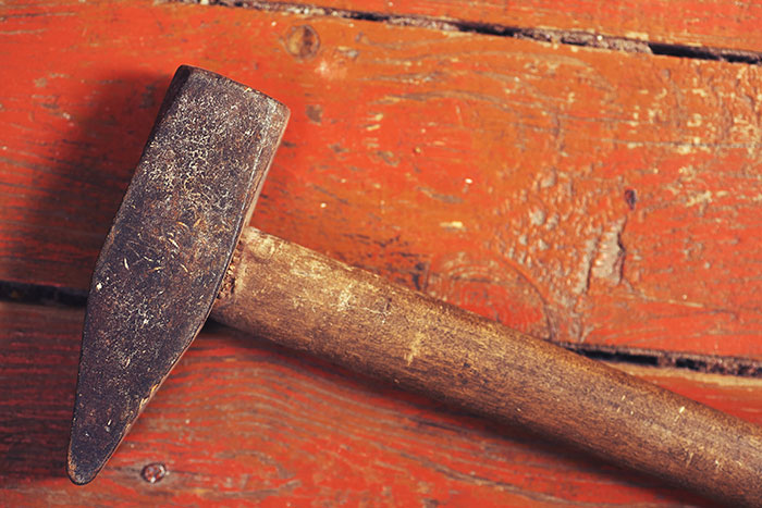 Rusty hammer on worn wooden surface, representing tools used by rage room customers needing therapy instead.