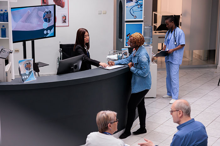 Patients checking in at a medical reception desk with a nurse and staff discussing therapy and treatment options.