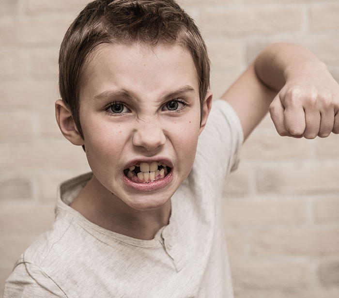 Angry child making a fist and snarling with aggression, illustrating rage room customers needing therapy instead.