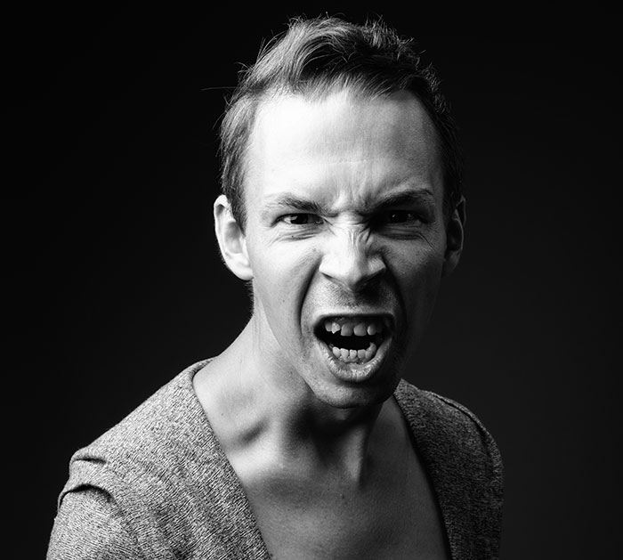 Young man expressing intense rage during a rage room session, showing emotions that suggest therapy might be needed.