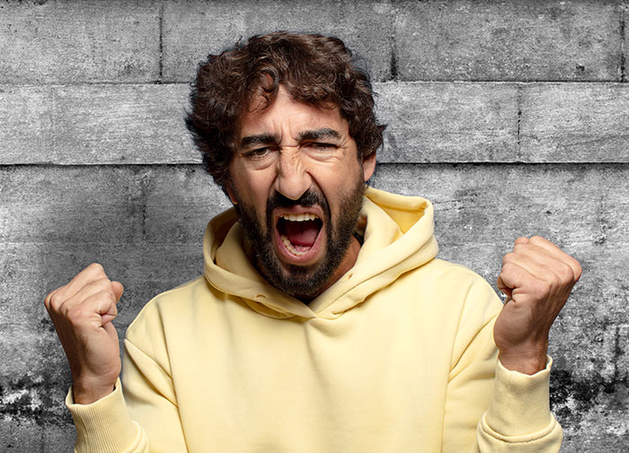 Man in yellow hoodie expressing rage and frustration, representing rage room customers needing therapy for anger management.
