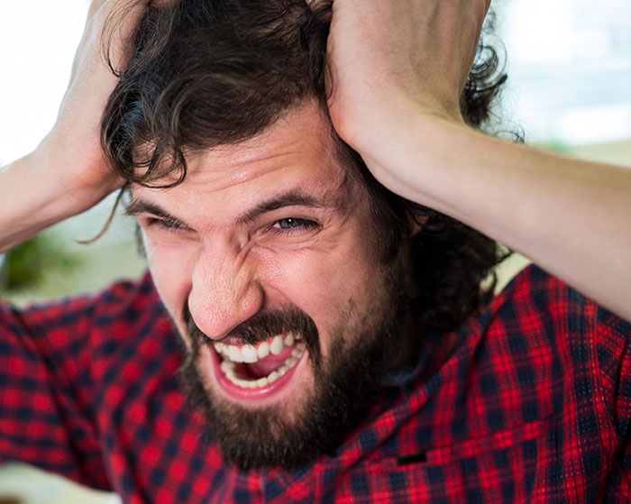 Man in red plaid shirt showing intense frustration, a common reaction from rage room customers needing therapy.