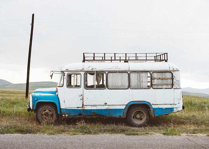 Old rusty blue and white bus parked on roadside in a remote grassy field, evoking a sense of real-life terror and paranoia.