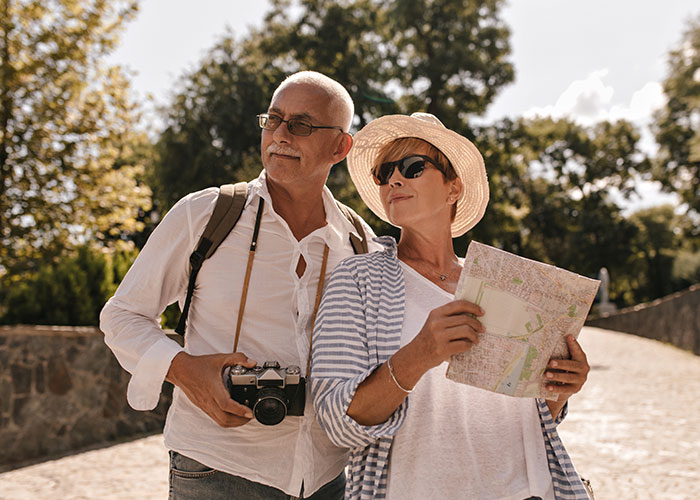 Middle-aged couple outdoors looking cautious while holding a camera and map, highlighting real-life terror and paranoia themes.