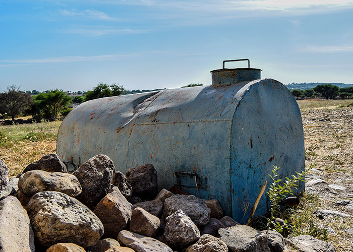 Old rusty metal tank surrounded by rocks in a rural area, illustrating times people faced real-life terror situations.