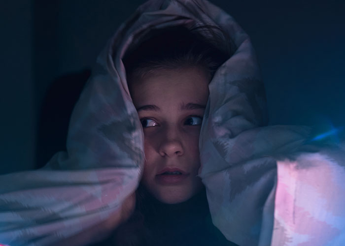 Young person hiding under a blanket at night, showing fear and paranoia facing real-life terror situations.