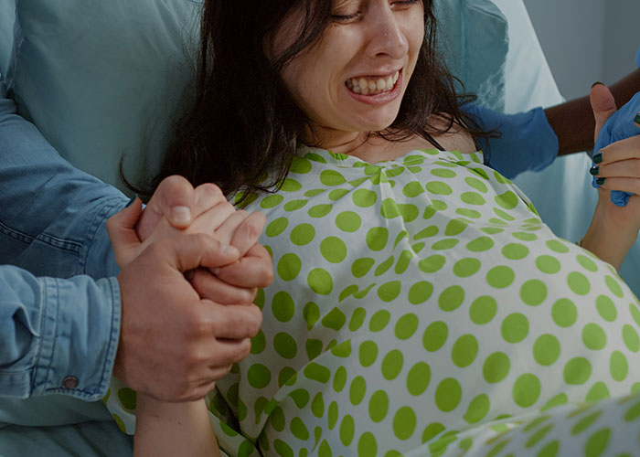 Pregnant woman in pain holding hands with support, experiencing real-life terror during childbirth in a hospital setting.