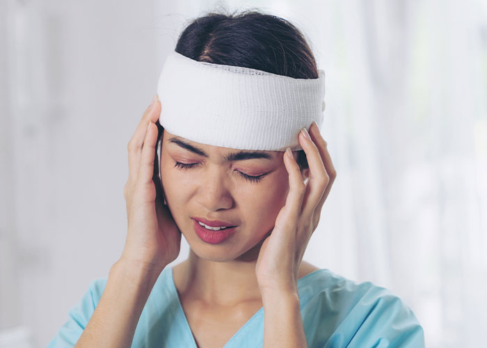 Young woman with head injury bandage touching temples, showing signs of real-life terror and distress in a medical setting