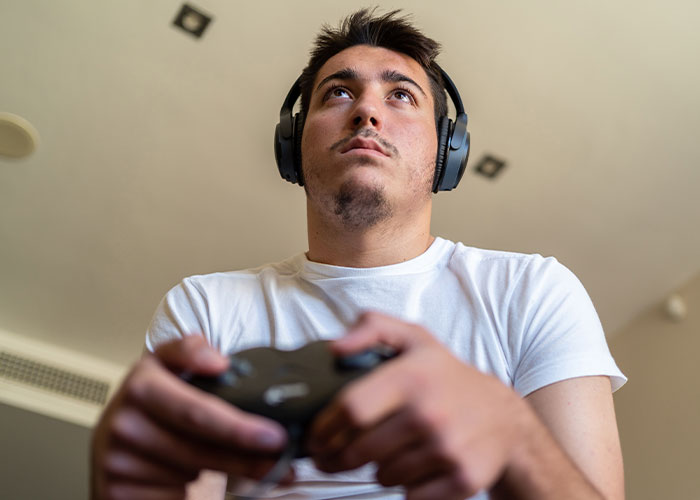 Young man wearing headphones, focused on video gaming, capturing a moment of real-life terror and paranoia.