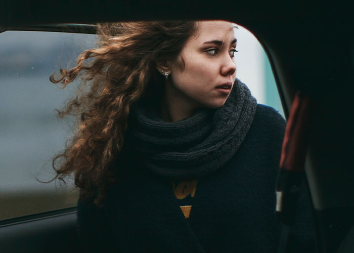 Young woman with curly hair looking outside a car window, capturing the feeling of real-life terror and paranoia.