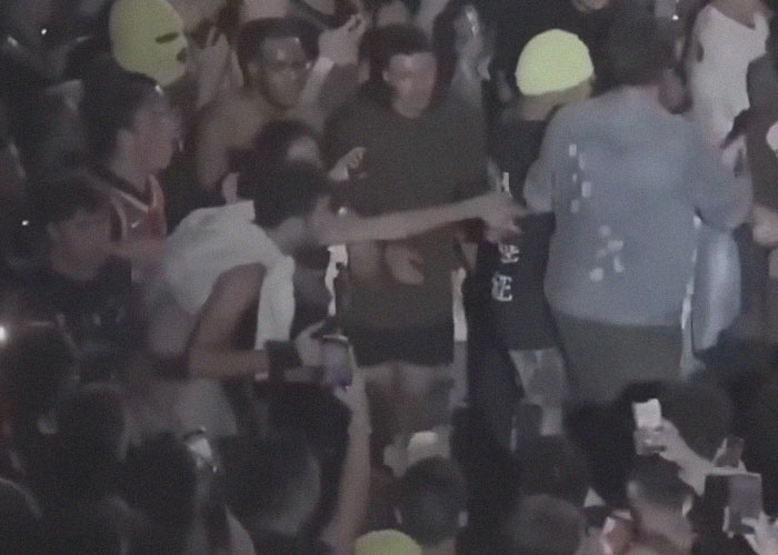 Crowd at night with people facing real-life terror, capturing moments with phones and reacting in disbelief.