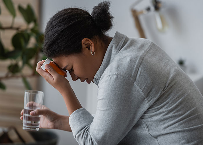 Woman feeling paranoid and distressed holding medication and glass of water in a home setting facing real-life terror situation.