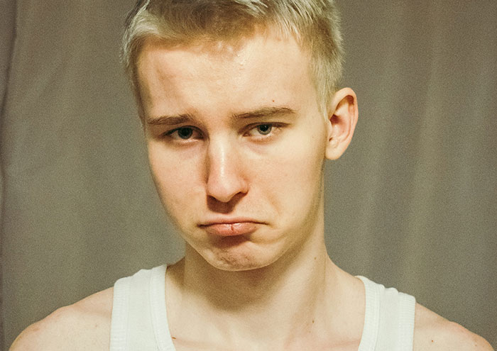 Young man with concerned expression wearing a white tank top relating to behaviors making women feel unsafe