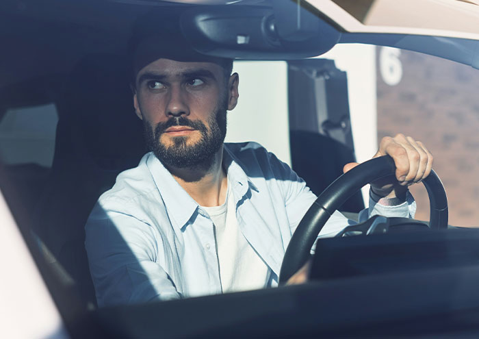 Man with a serious expression driving a car, highlighting behaviors from men that might make women feel unsafe.