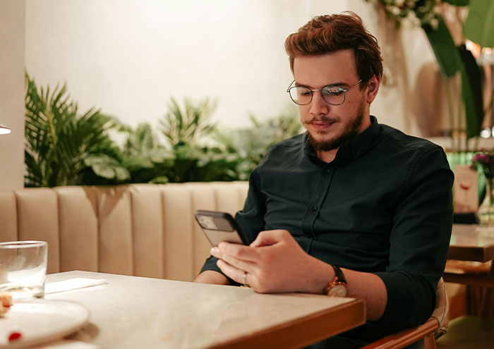 Man sitting alone at a table, looking at his phone, illustrating behaviors from men that might make women feel unsafe.