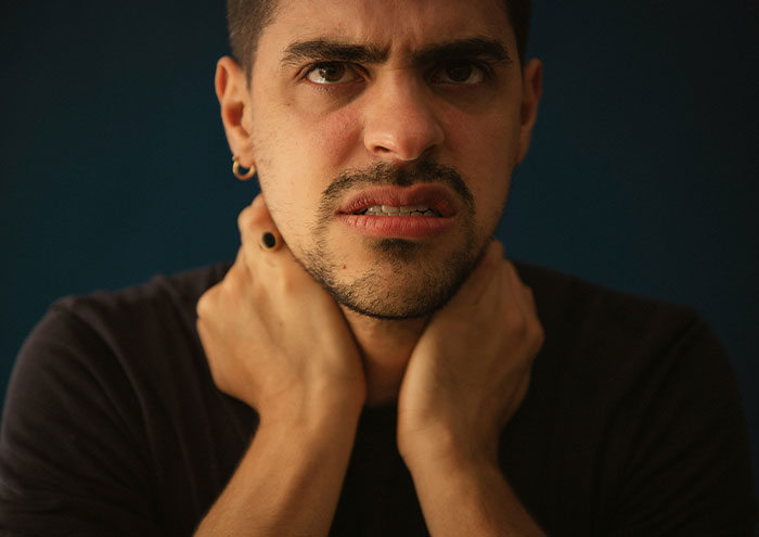 Close-up of a man with a concerned expression, clutching his neck, illustrating behaviors that might make women feel unsafe.