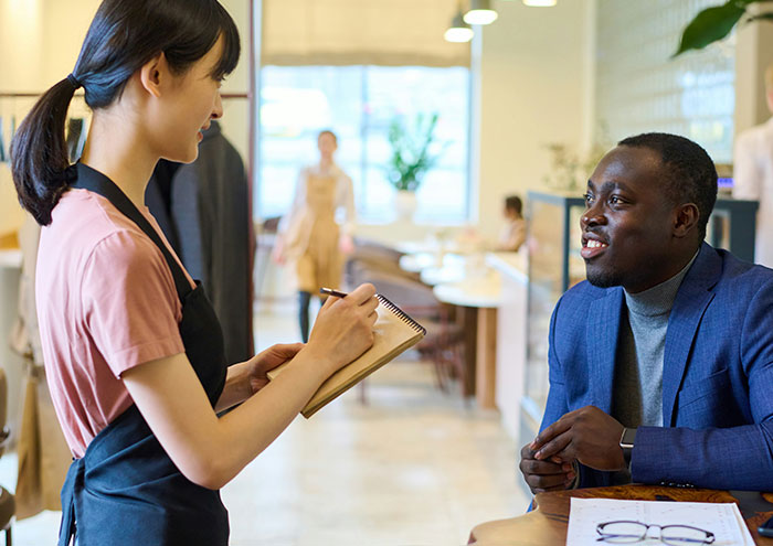 Woman waitress taking order from man at café, highlighting behaviors from men that might make women feel unsafe.