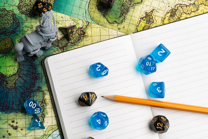 Blue and black dice with a pencil on an open notebook over a detailed fantasy game map and miniature figure.