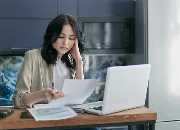 Young woman reviewing documents at a table, concerned about elderly parents expecting daughter to support them financially. Young woman reviewing documents at a table, concerned about elderly parents expecting daughter to support them financially.
