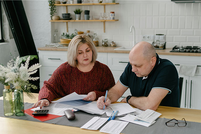 Elderly parents reviewing finances with documents and calculator, expecting daughter to support after business losses. Elderly parents reviewing finances with documents and calculator, expecting daughter to support after business losses.