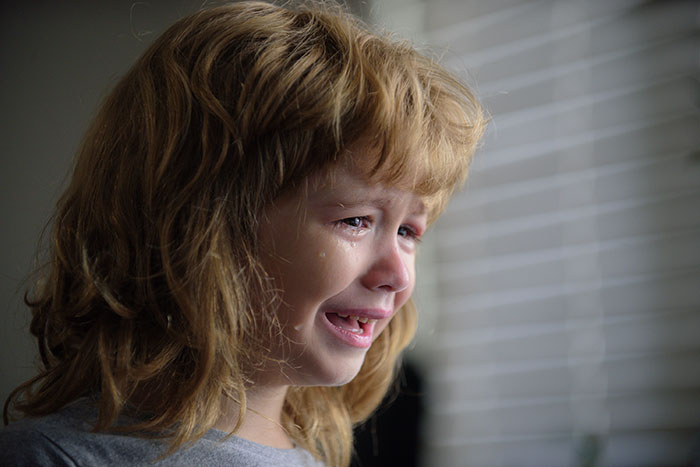 Crying child with tears running down their cheek, conveying fear and distress related to growing up with a psychopath.