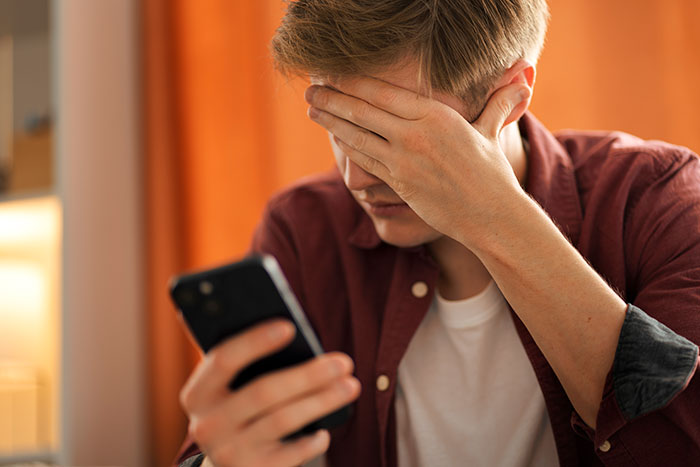 Young man holding phone looking distressed, depicting experiences of people who grew up with a psychopath.