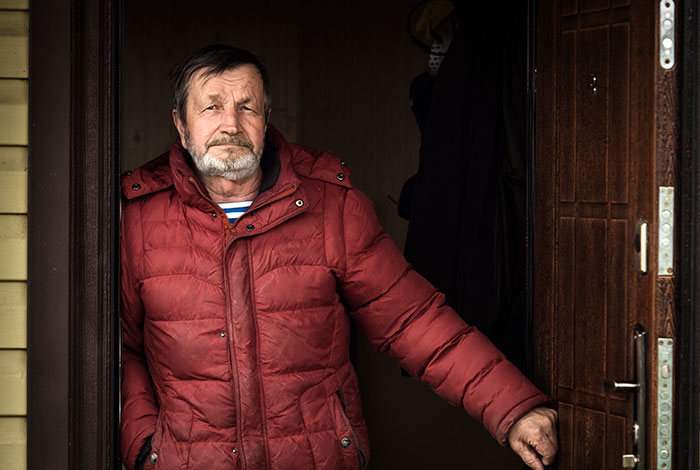 Older man in red jacket standing at a doorway, representing people who grew up with a psychopath in their life.
