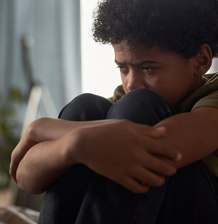 Sad young boy sitting curled up, reflecting the emotional impact of growing up with a psychopath experiences.