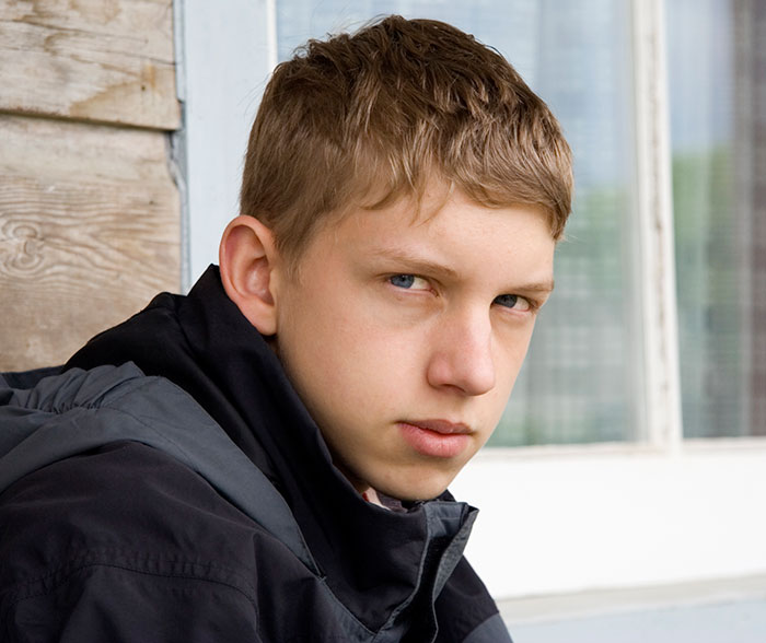 Teenage boy with serious expression sitting outside, conveying emotions related to growing up with a psychopath.