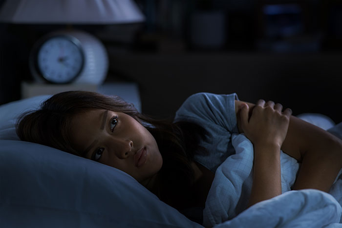 Woman lying awake in bed at night, appearing anxious and troubled, reflecting experiences with a psychopath in childhood.