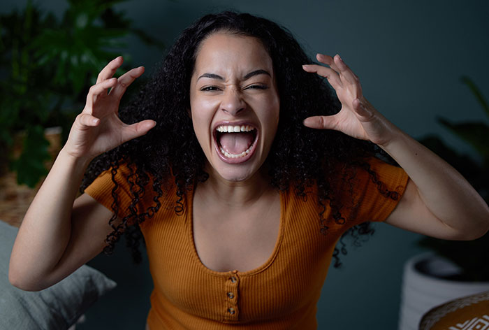 Woman in an orange top screaming with hands raised, expressing intense emotion linked to growing up with a psychopath experience