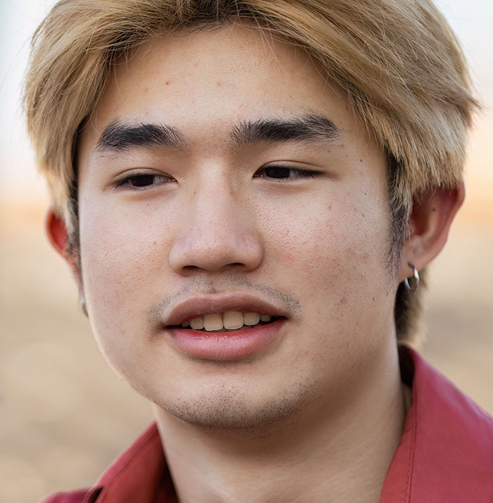 Young man with blonde hair and earrings looking away thoughtfully, reflecting on experiences with a psychopath.