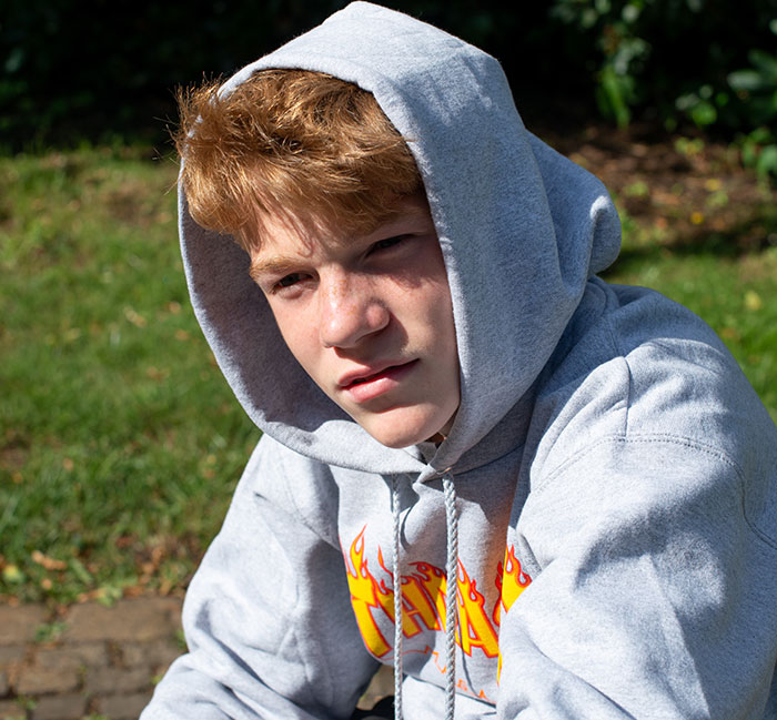 Teen boy wearing a gray hoodie sitting outdoors, reflecting on experiences with a psychopath during his upbringing.