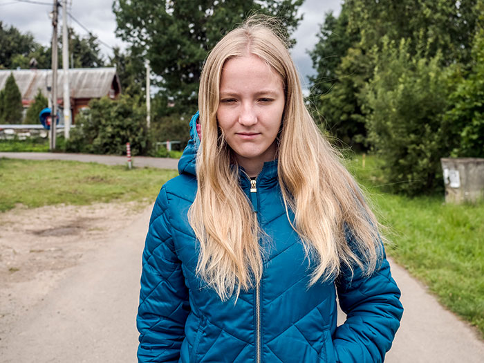 Young woman in a blue jacket standing outside, appearing thoughtful, reflecting on experiences with a psychopath in childhood.