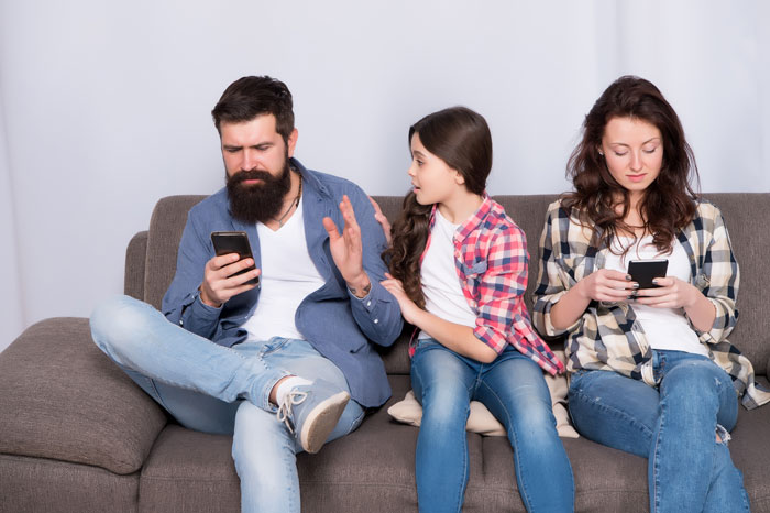 Father ignoring daughter while sister and mom use phones on couch showing relationship siblings sister mom dynamics.