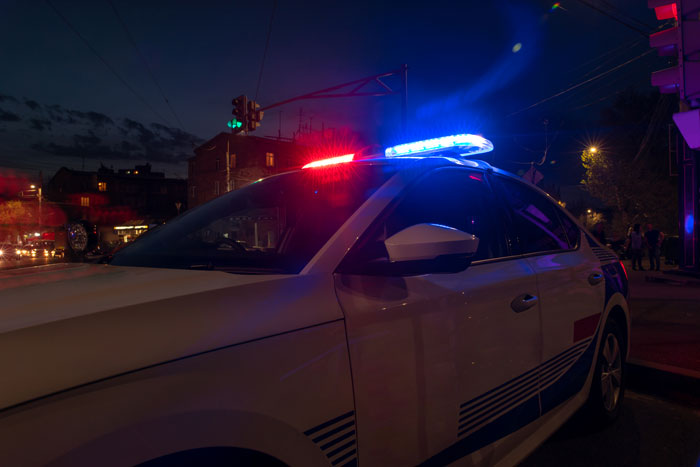 Police car with flashing lights at night, symbolizing response to domestic violence accusations and emotional distress.