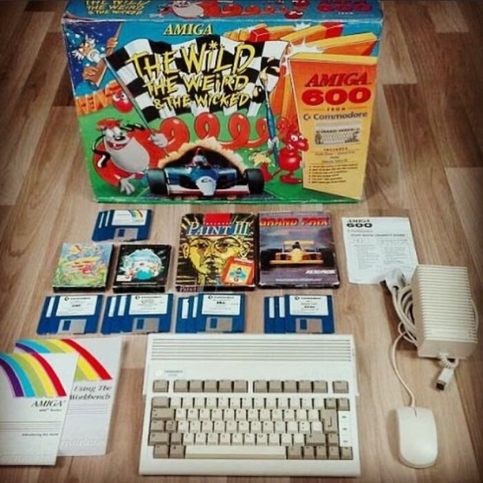 Vintage Amiga 600 computer with games, floppy disks, and manuals laid out on a wooden floor showcasing retro gaming nostalgia.