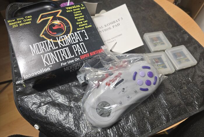 Retro gaming accessories including a Mortal Kombat 3 controller and classic Super Nintendo game cartridges on a table.
