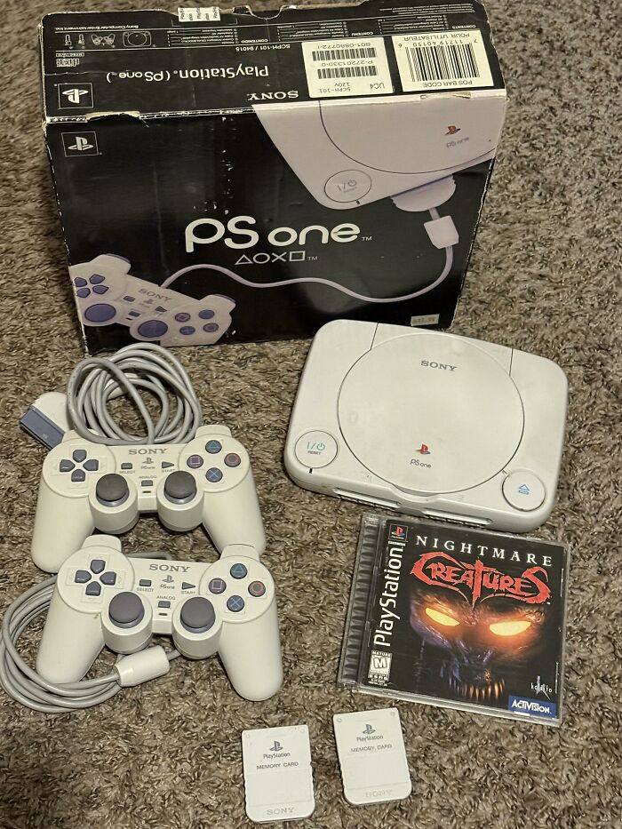 Sony PlayStation PS One console with two controllers, memory cards, and Nightmare Creatures game, retro gaming nostalgia setup.