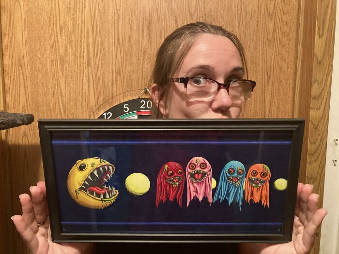 Person holding a framed artwork of retro gaming characters with a dark background and wooden wall behind.