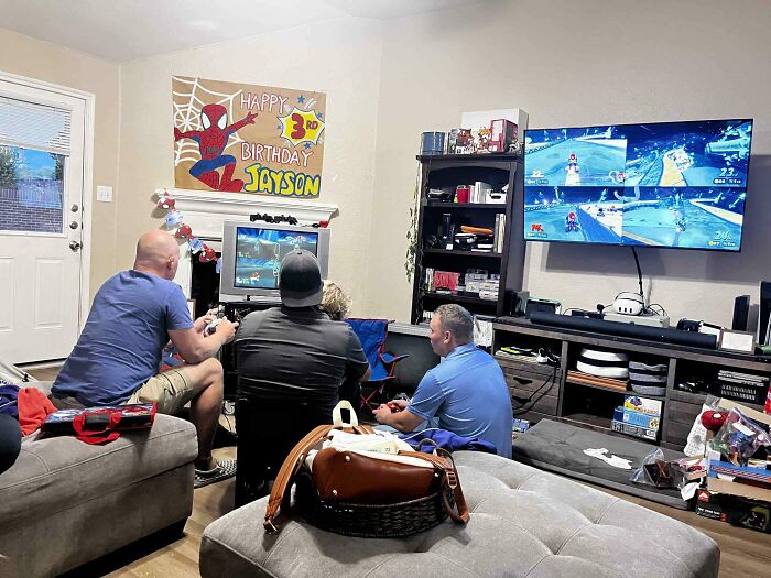 Three men playing retro gaming together in a cozy living room filled with nostalgic gaming consoles and decor.