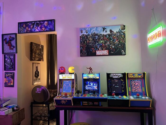 Retro gaming arcade setup with vintage machines, Pac-Man figures, and Marvel posters creating nostalgic ambiance.