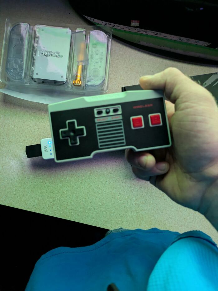 Hand holding a retro gaming controller resembling an 80s console, with nostalgic gaming accessories on a desk.