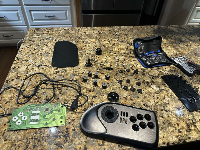 Disassembled retro gaming controller parts laid out on a granite countertop with tools nearby for restoration and nostalgia.