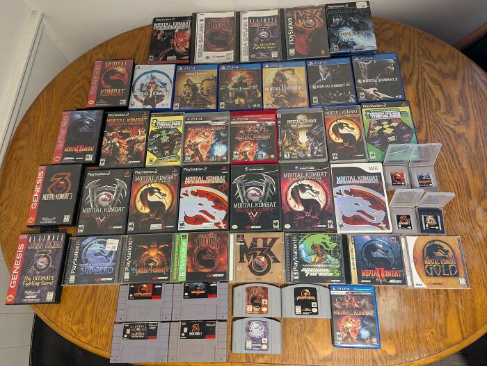 Collection of retro gaming Mortal Kombat video games from various consoles on a wooden table showcasing nostalgia for 80s, 90s, and 00s.
