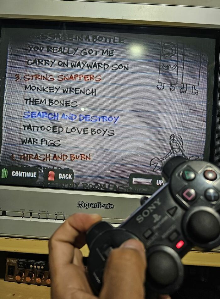 Person holding a Sony PlayStation controller playing a retro gaming music game on an old CRT TV screen.