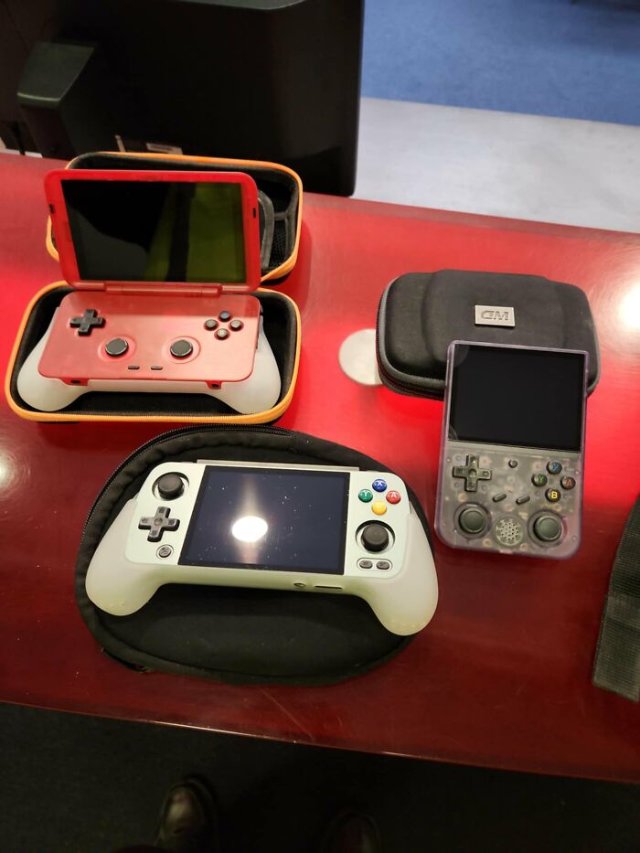 Three retro gaming handheld consoles on a red table, showcasing nostalgia with classic controller designs and cases.