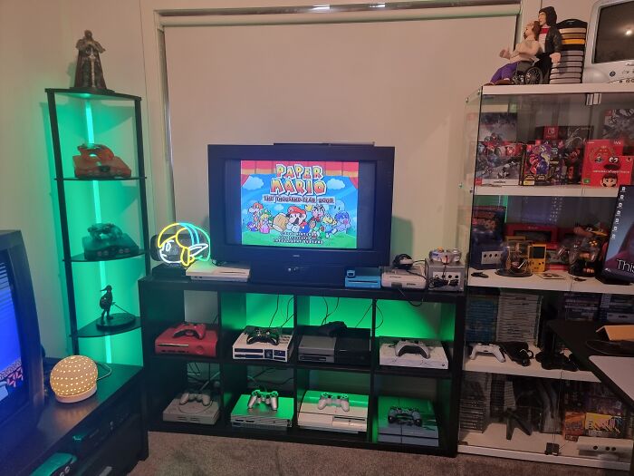 Retro gaming setup with classic consoles, controllers, and nostalgic video games displayed on shelves and TV.